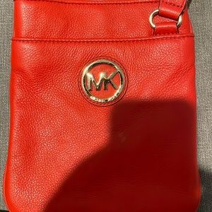 A red Micheal kors bag that is a crossbody